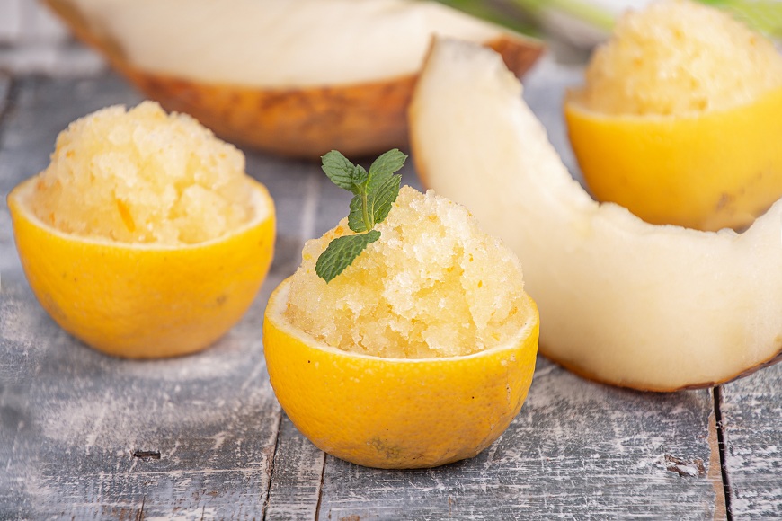 Jak připravit domácí zmrzlinu se zmrzlinovačem i bez něj Citronový sorbet servírovaný v citronové slupce. V pozadí je žlutý meloun.