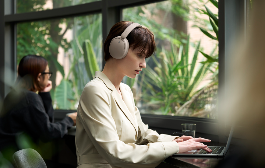 Sony představuje nová sluchátka. Kombinují styl, pohodlí, ANC, dlouhou výdrž a kvalitní zvuk v moderním designu Žena sedí v kavárně u počítače a na uších má sluchátka Sony.