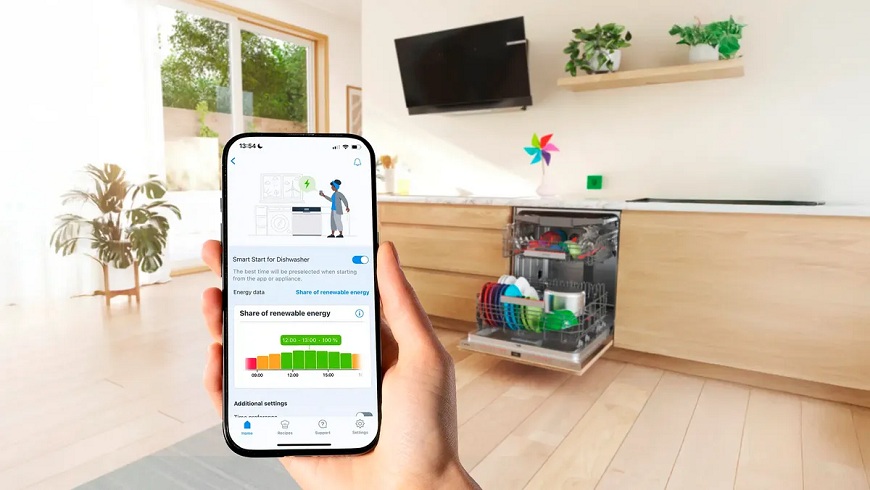 Co je Smart Start u chytrých spotřebičů Bosch? Ruka držící mobil s otevřenou funkcí Smart start, v pozadí myčka Bosch