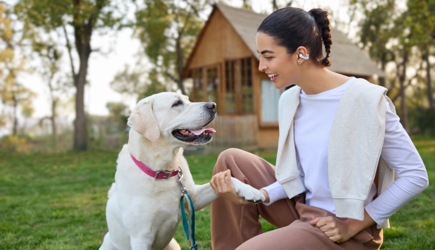 Shokz OpenDots 2 a OpenDots Air: Otevřená sluchátka, která vás neodříznou od okolí Žena si hraje se psem a má sluchátka Shokz OpenDots 2
