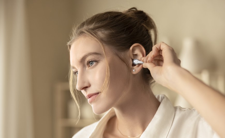 Shokz OpenDots 2 a OpenDots Air: Otevřená sluchátka, která vás neodříznou od okolí Žena si nasazuje otevřené sluchátko OpenDots 2 Shokz