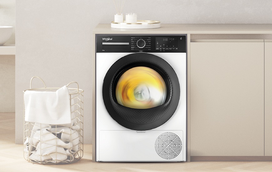 Sychravý podzim sušení prádla nepřeje. Sušičky Whirlpool ano! Sušička Whirlpool s bubnem plným prádla. Vedle sušičky je koš na prádlo.