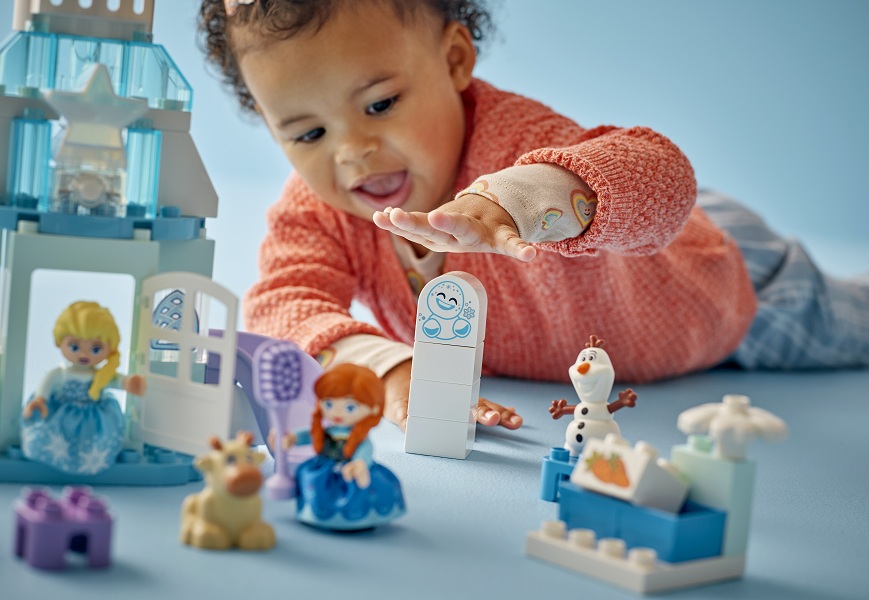 Malá holčička si hraje na zemi se stavebnicí LEGO® DUPLO® Disney 10455 Ledové království: Anna a Elsa a oslava na hradě.
