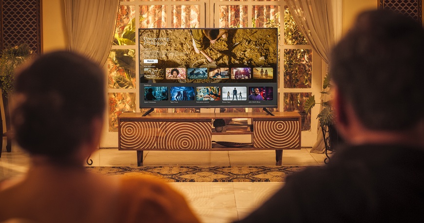 75, 98 nebo 115 palců? Rozdíl, který musíte vidět naživo! Žena a muž sedí před televizí v obýváku.